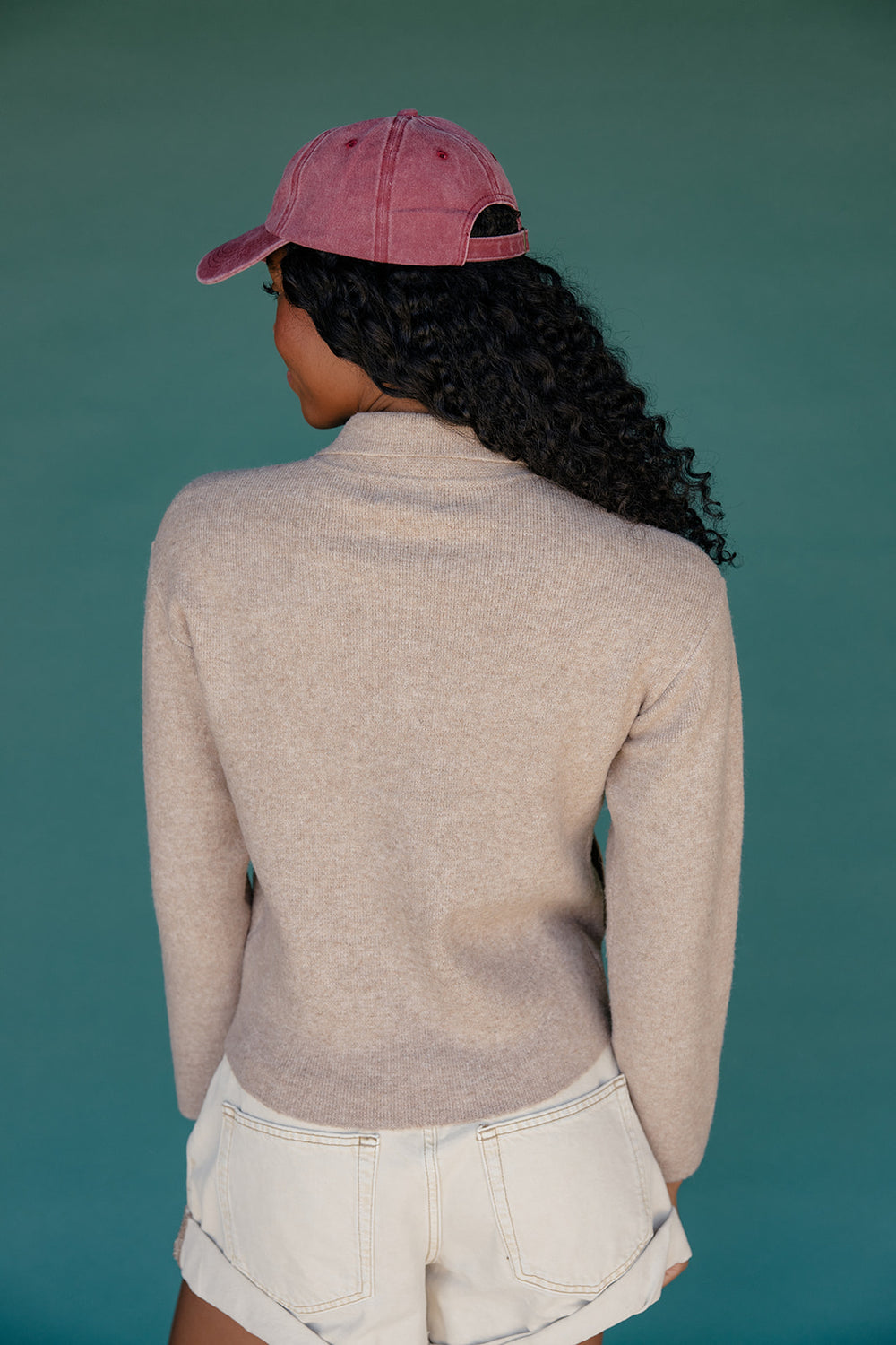 Person wearing a pink cap and beige sweater against a teal background