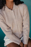 Person wearing a beige cardigan over a white shirt against a teal background
