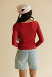 Person wearing a red long-sleeve top and denim shorts with a beige headscarf on a beige background