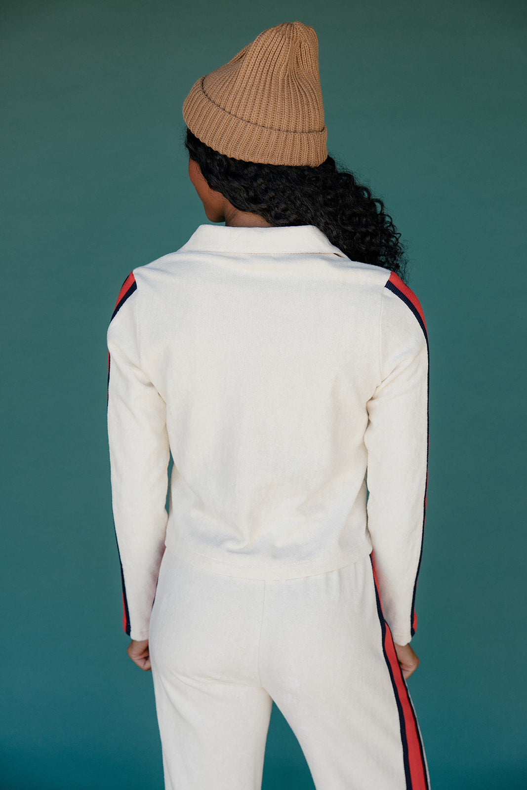 Person wearing a white outfit with red and black stripes on a teal background