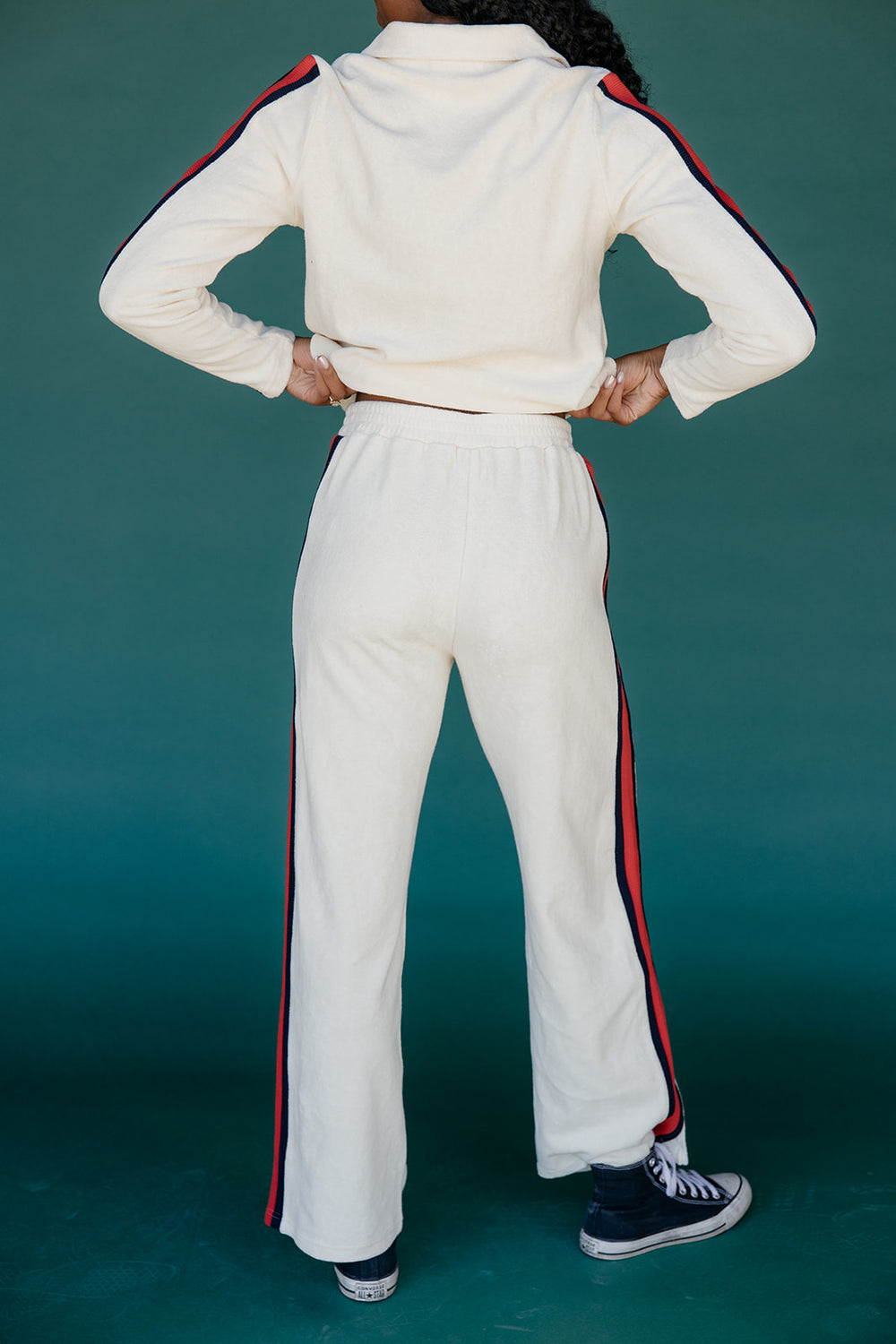 Person wearing a white tracksuit with red and blue stripes on a teal background