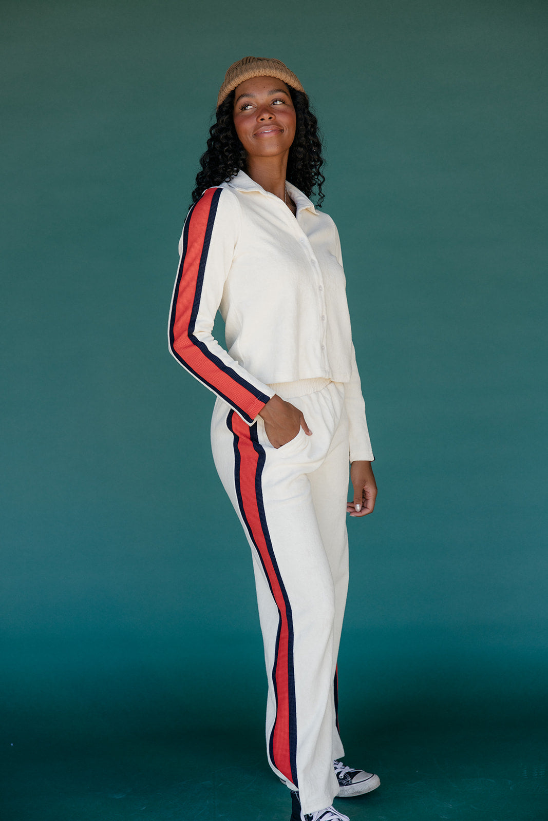 Person wearing a white tracksuit with red and blue stripes against a teal background
