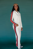 Person wearing a white tracksuit with red and blue stripes against a teal background