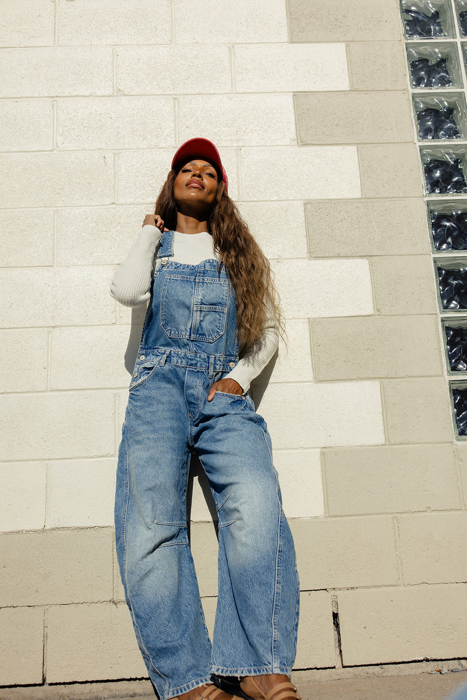 a woman in overalls leaning against a wall