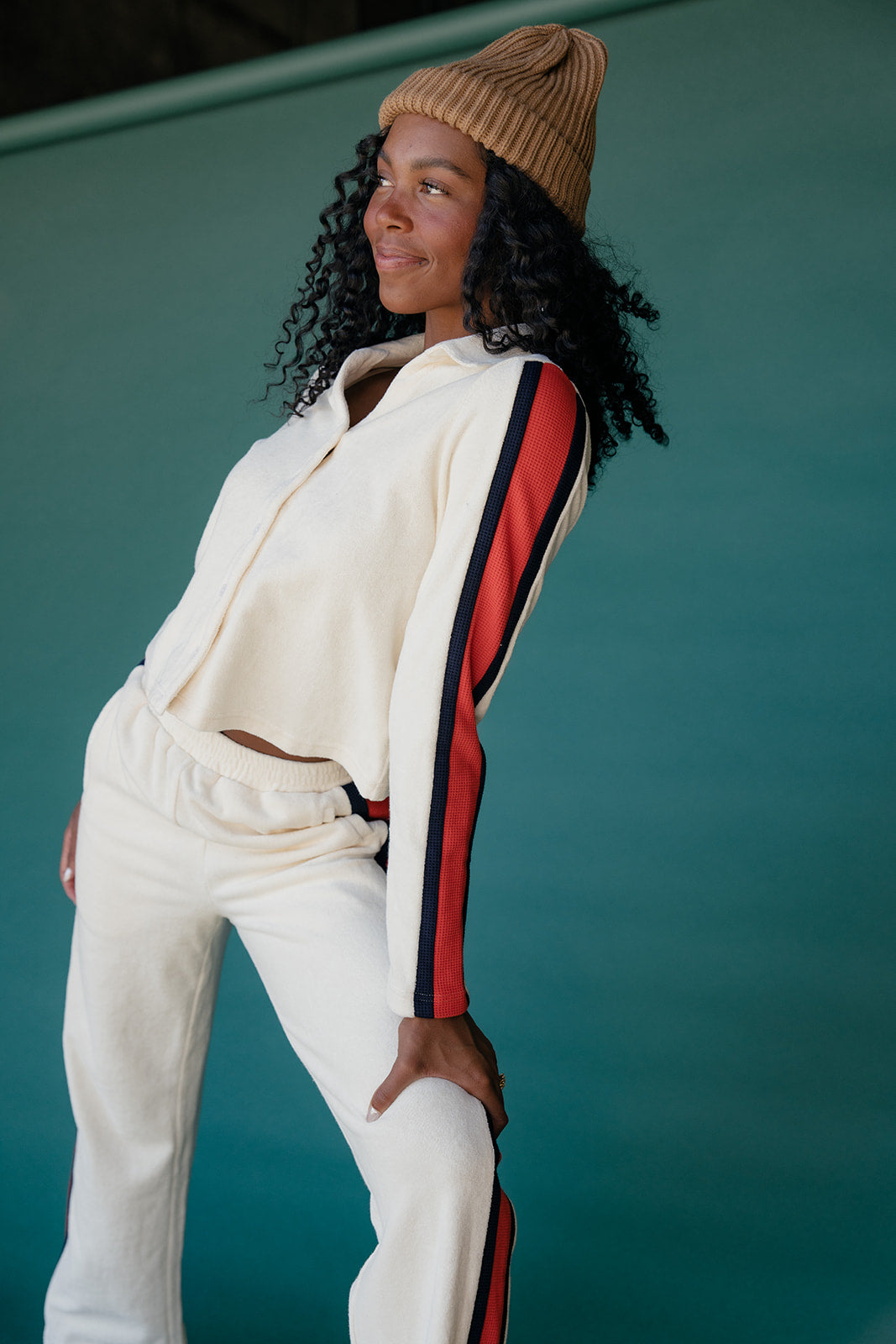 Person wearing a white tracksuit with red and blue stripes against a teal background
