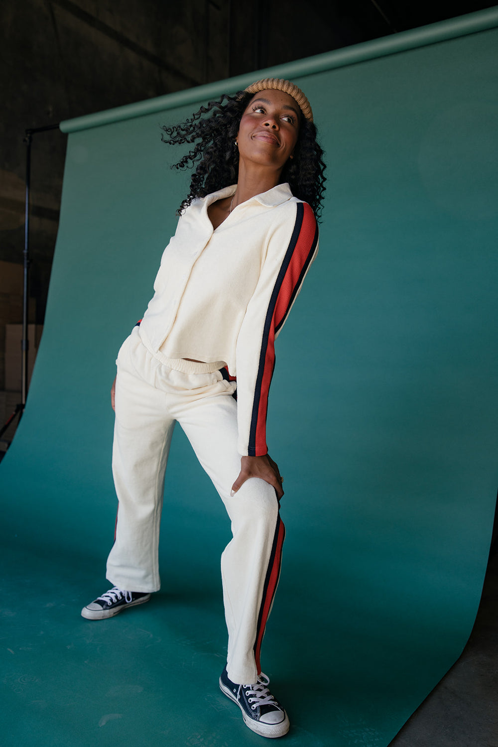 Person wearing a white tracksuit with red and blue stripes against a teal backdrop