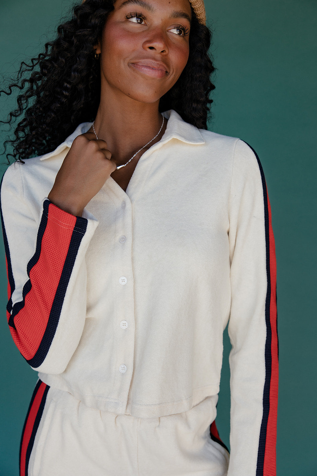 Woman wearing a cream-colored outfit with red and navy accents against a teal background