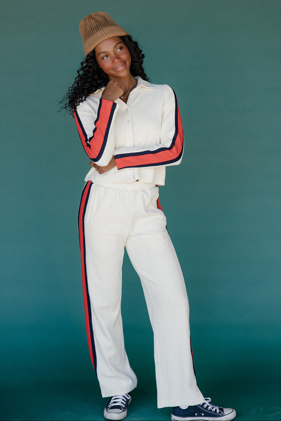 Woman wearing a white outfit with red and blue accents against a teal background