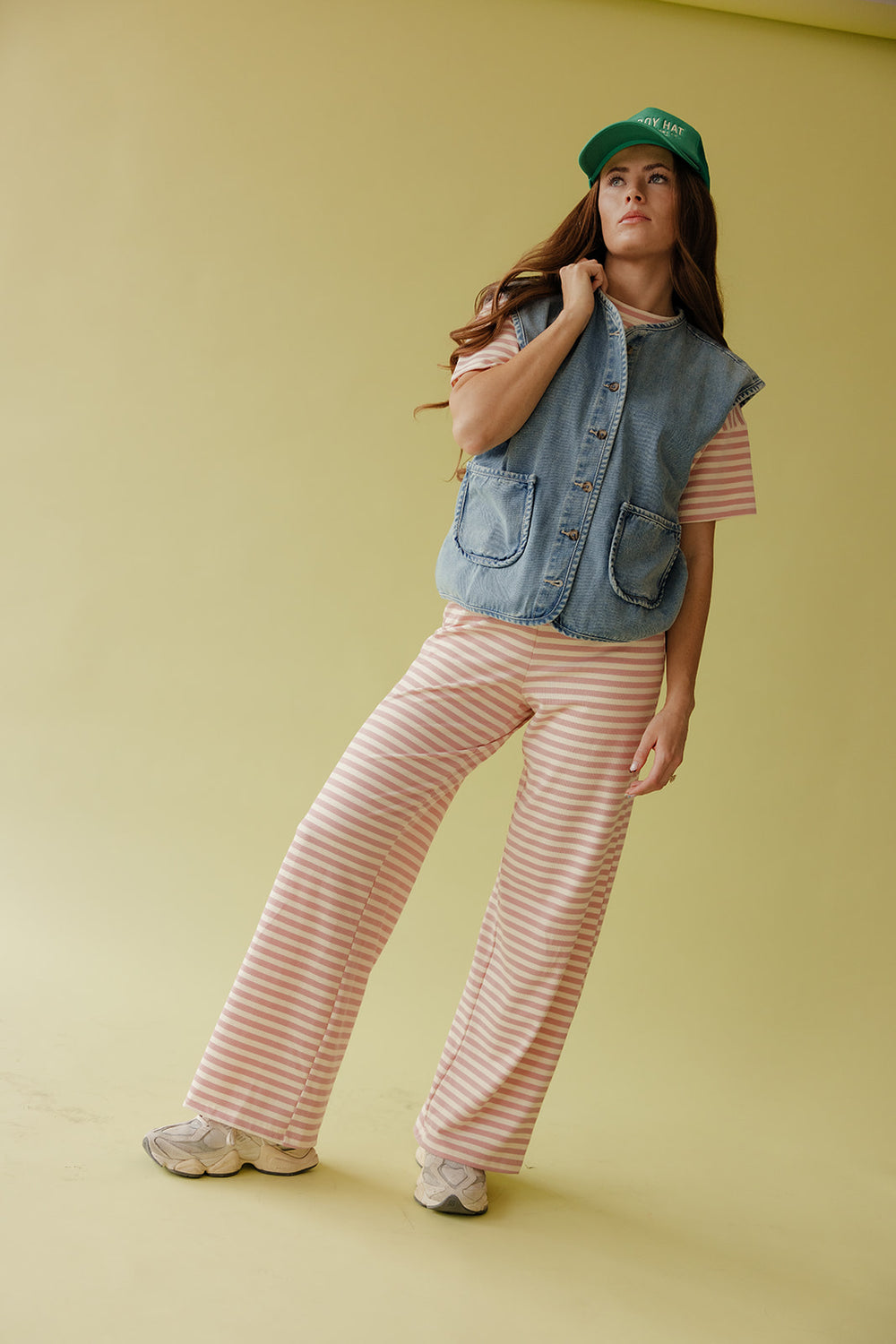 Person wearing a denim vest, striped pants, and a green cap against a yellow background