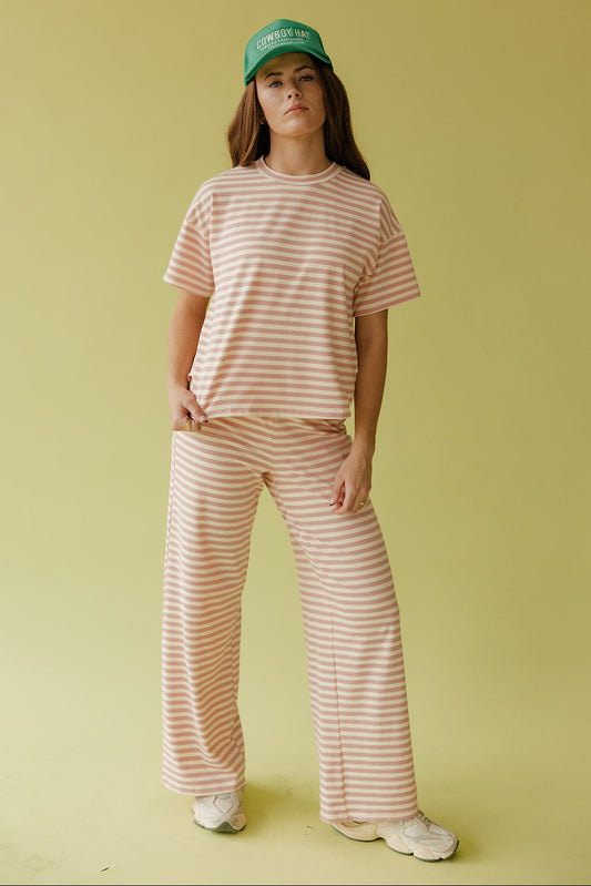 Person wearing a striped pink and white outfit with a green cap on a yellow background