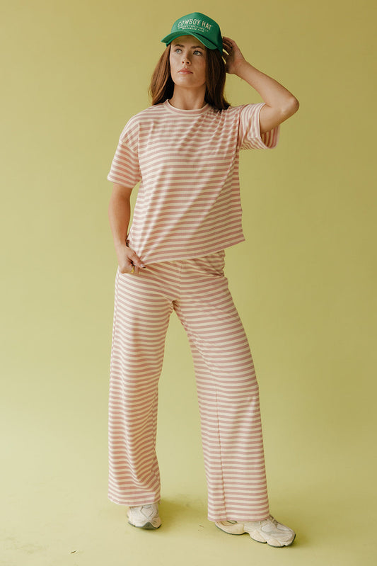 Person wearing a striped pink and white outfit with a green cap on a yellow background