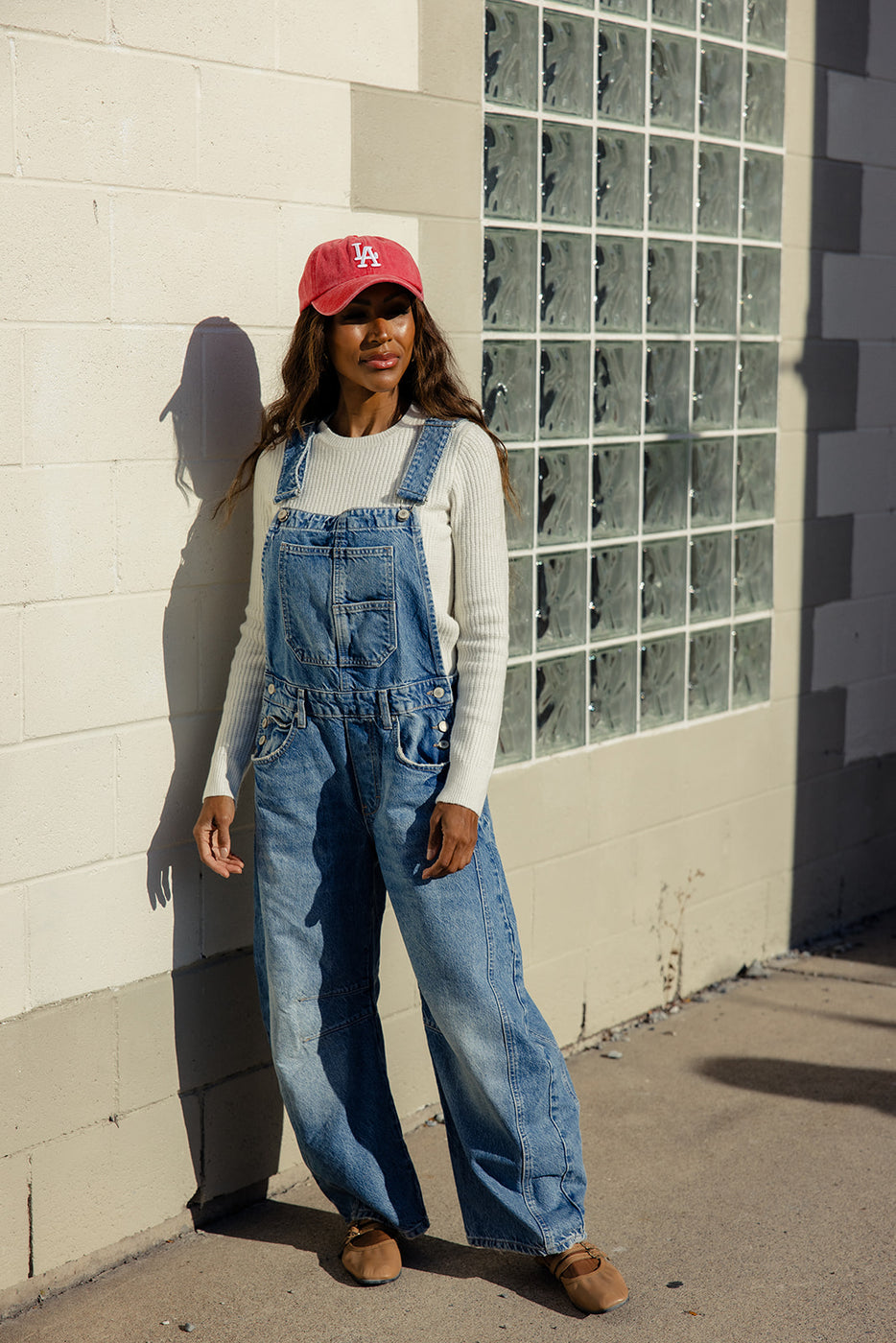 a woman in overalls and a red hat standing by a wall