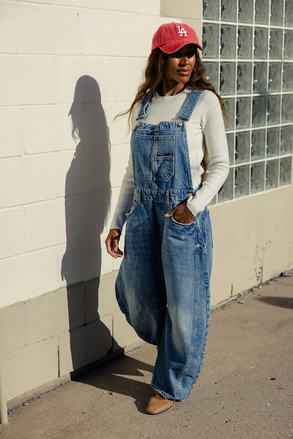 a woman in overalls standing by a wall