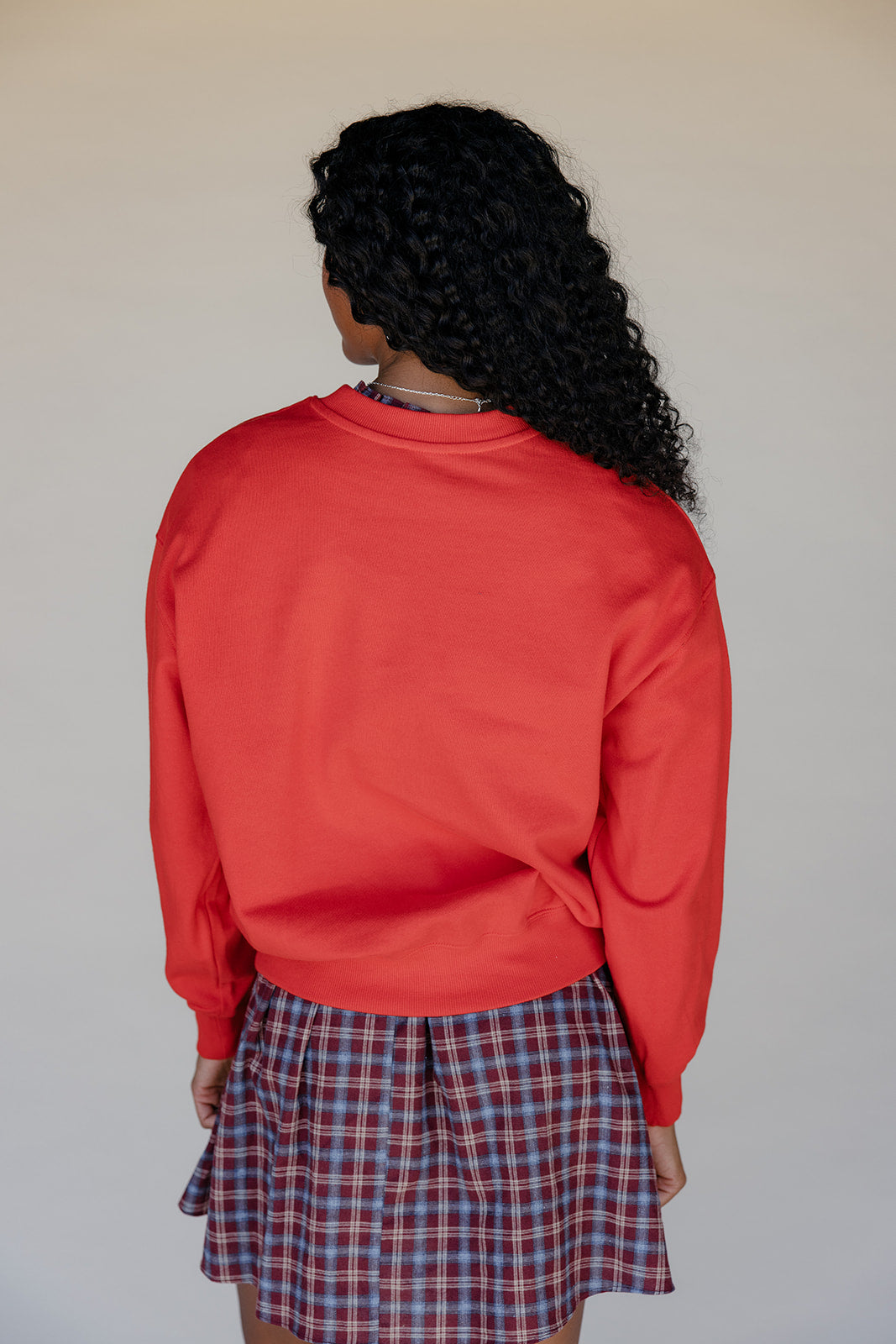 Person wearing a red sweatshirt and plaid skirt against a plain background