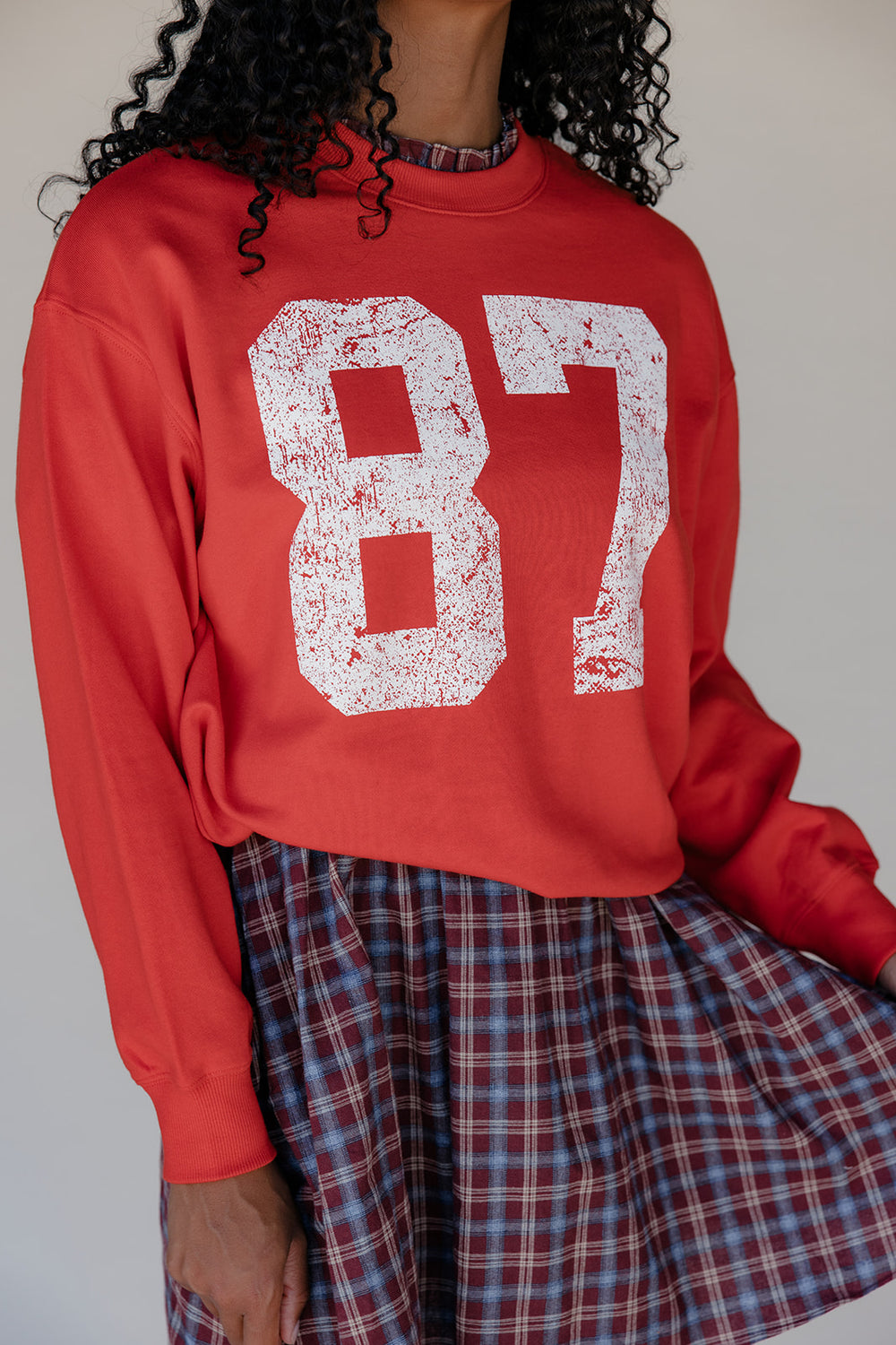 Person wearing a red sweatshirt with the number 87 printed on it, standing against a plain background.