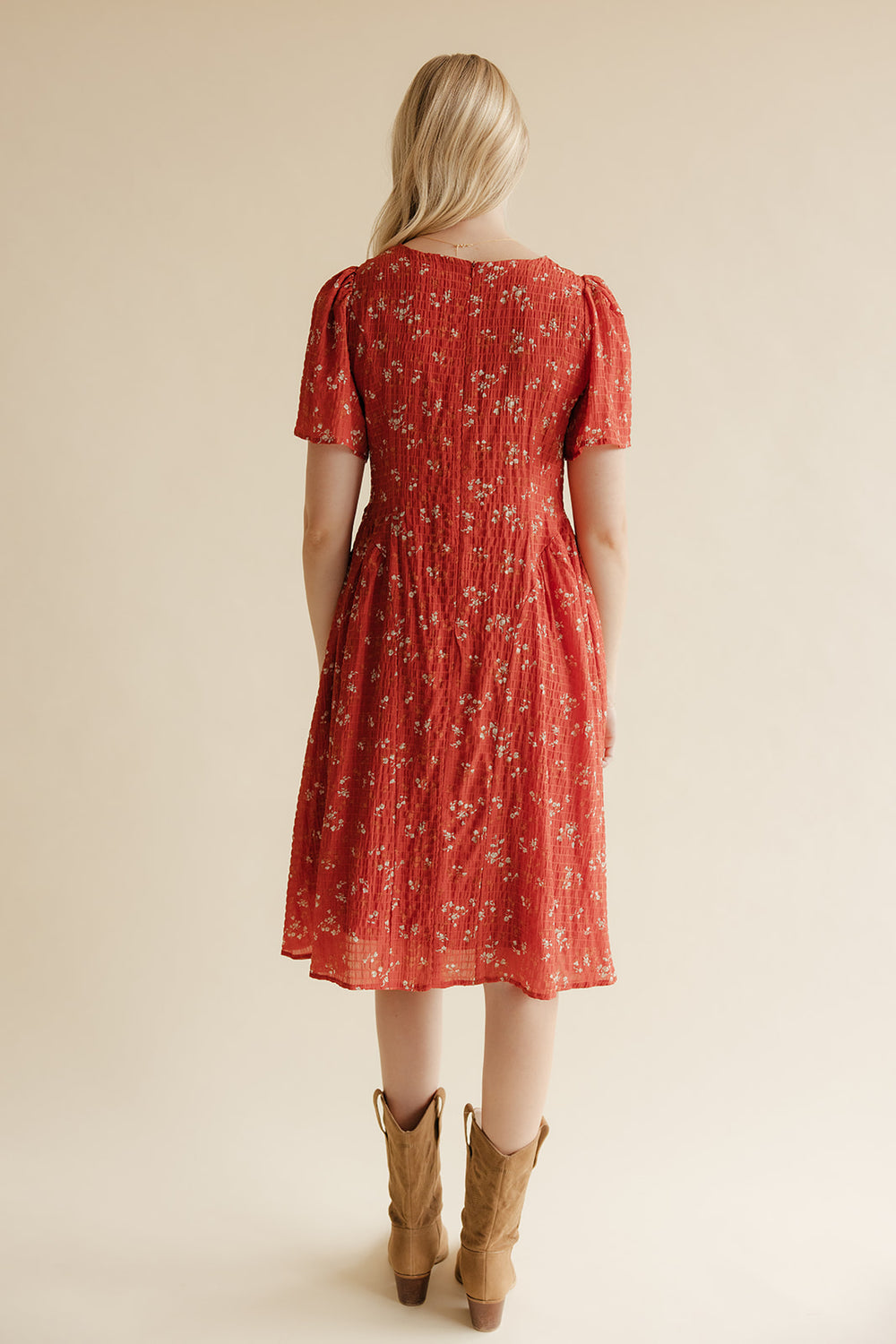 Woman wearing a red floral dress with brown boots on a beige background