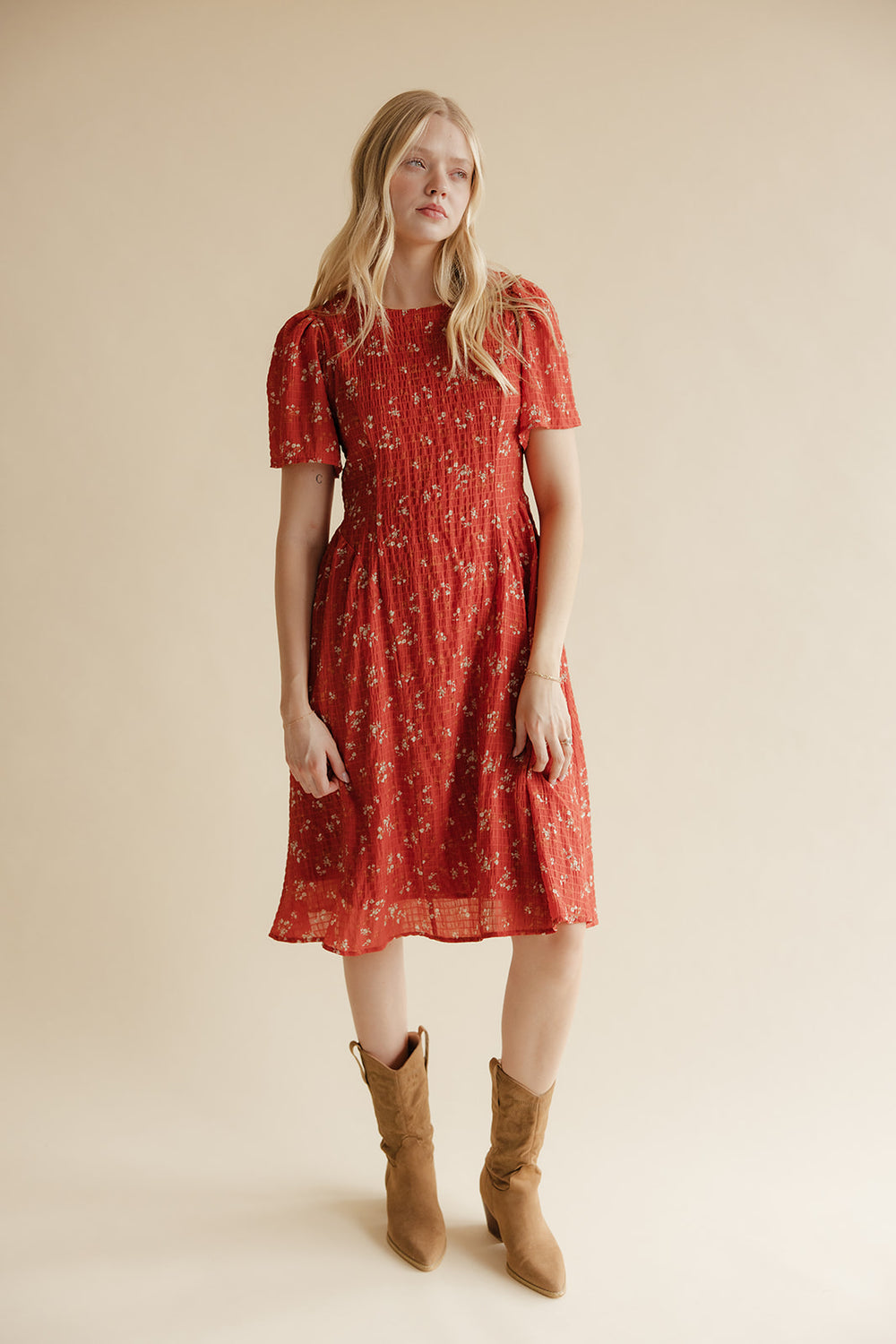 Woman wearing a red floral dress and brown boots on a beige background