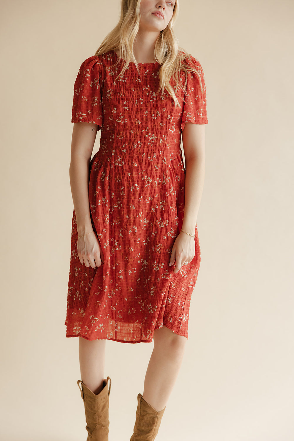 Woman wearing a red floral dress with brown boots on a beige background