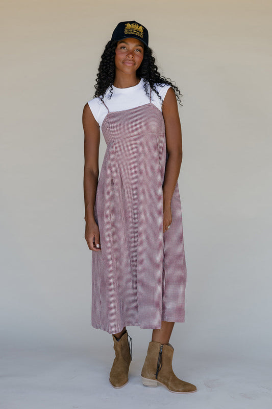 Woman wearing a pink dress over a white shirt, standing against a plain background