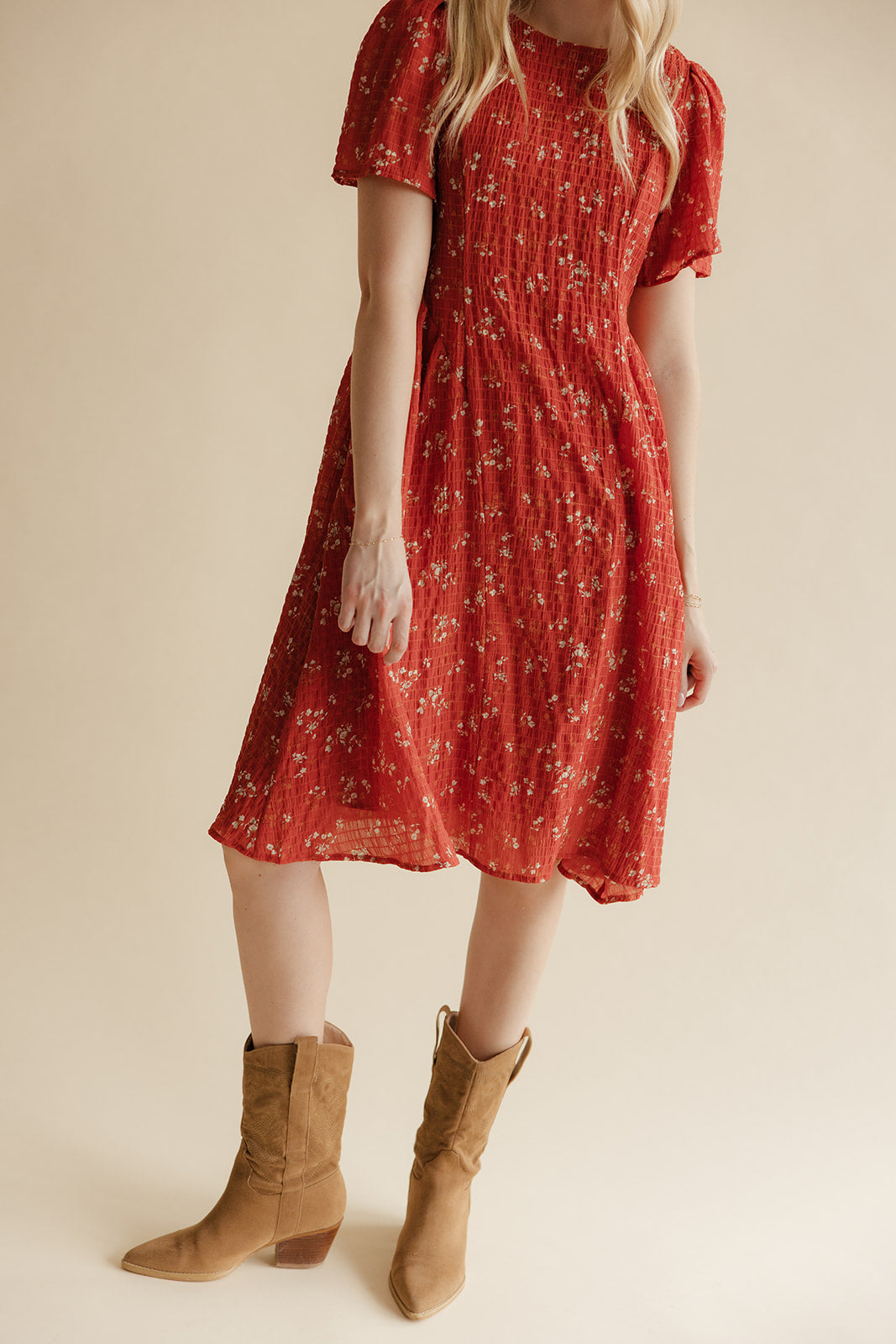 Person wearing a red floral dress with brown boots on a beige background