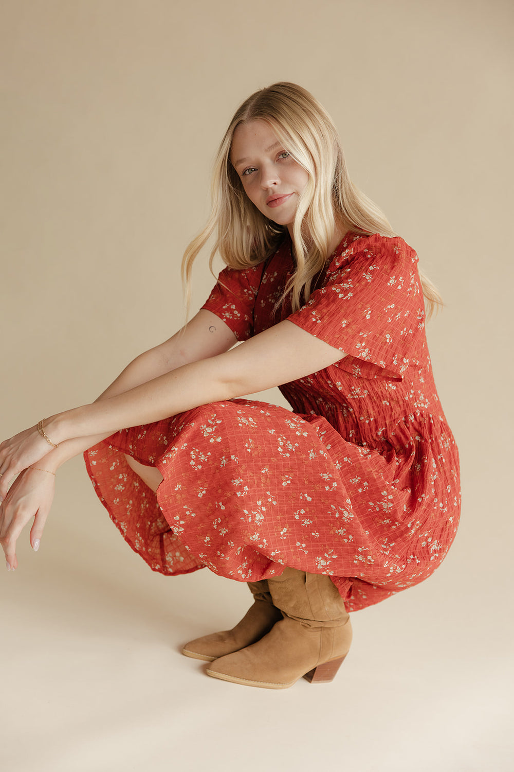 Woman in a red floral dress and brown boots sitting on a beige background