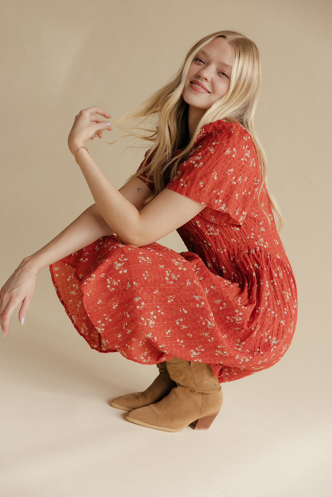 Woman in a red floral dress and brown boots posing on a beige background