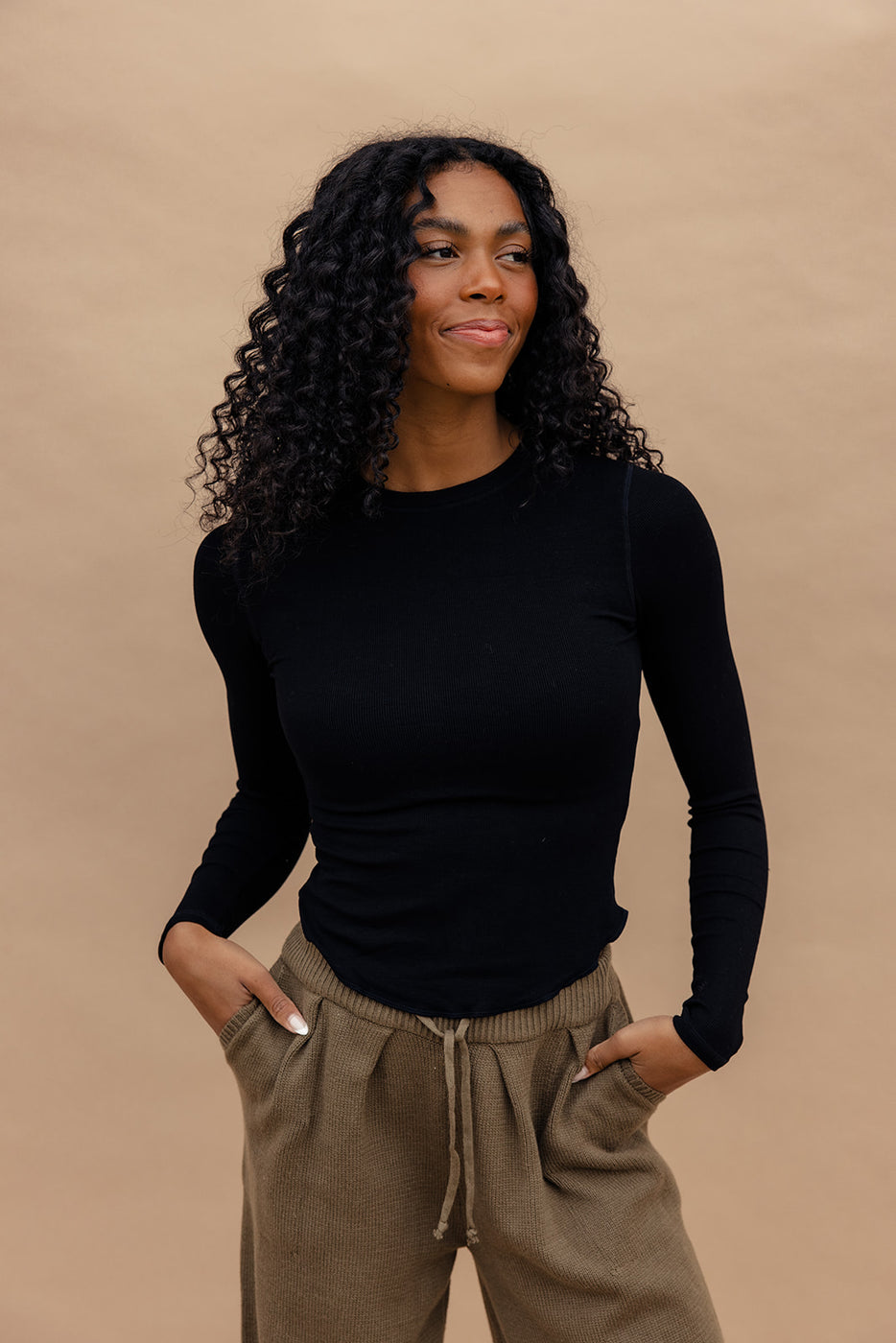 a woman with long curly hair wearing a black shirt and brown pants