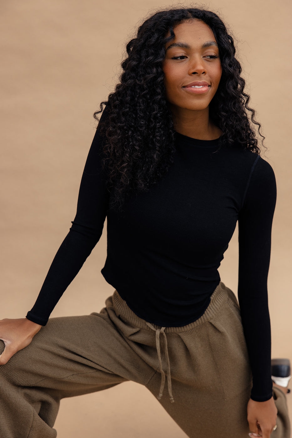 a woman with long curly hair wearing a black shirt and brown pants