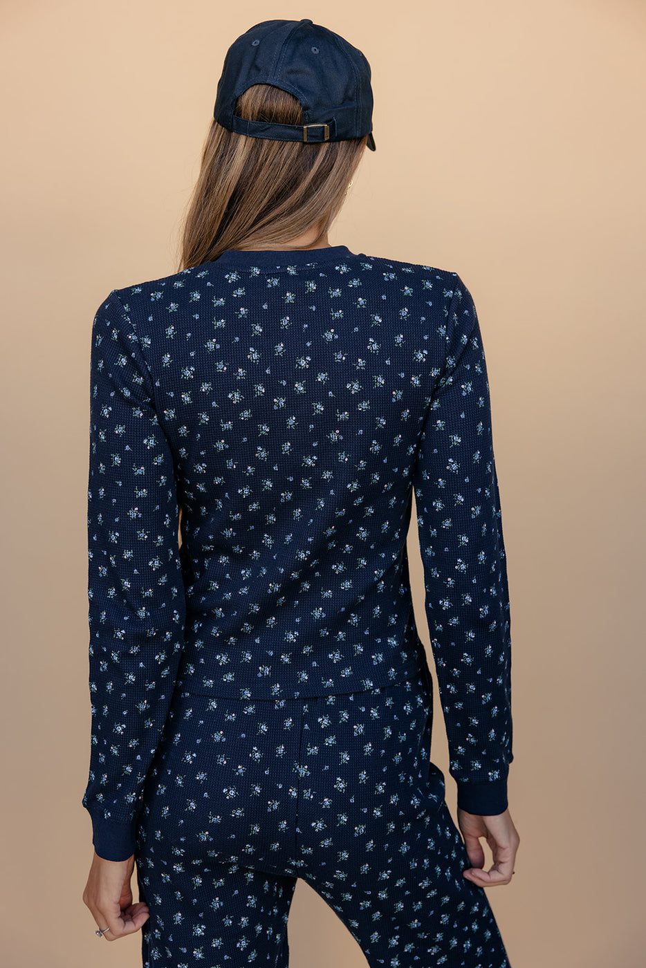 Person wearing a navy blue long-sleeve top with white patterns and matching pants on a beige background.