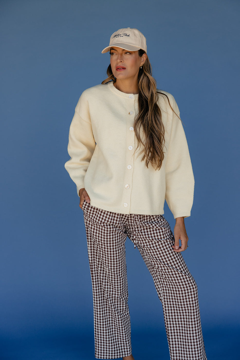 Woman wearing a cream cardigan and checkered pants against a blue background