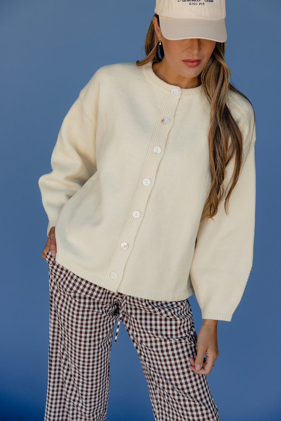 Person wearing a cream cardigan and checkered pants against a blue background