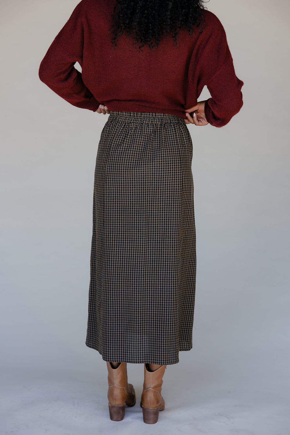 Person wearing a red sweater and plaid skirt against a plain background