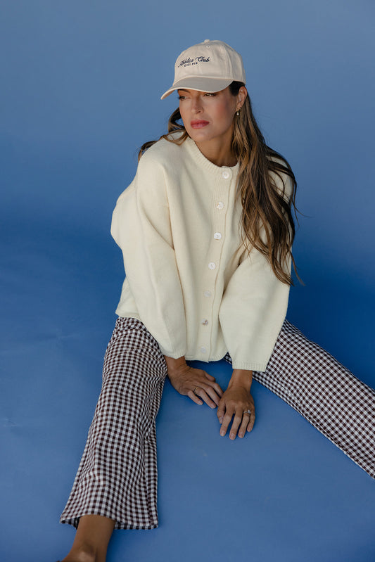 Woman wearing a white cardigan and checkered pants sitting against a blue background