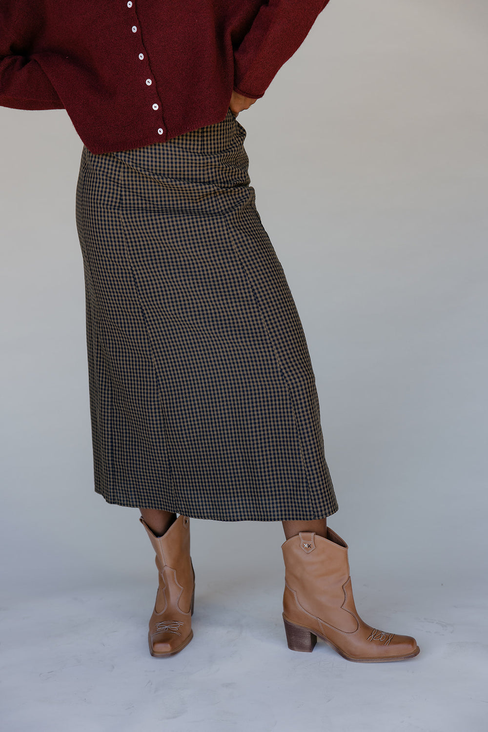Person wearing a red shirt, plaid skirt, and brown boots on a plain background