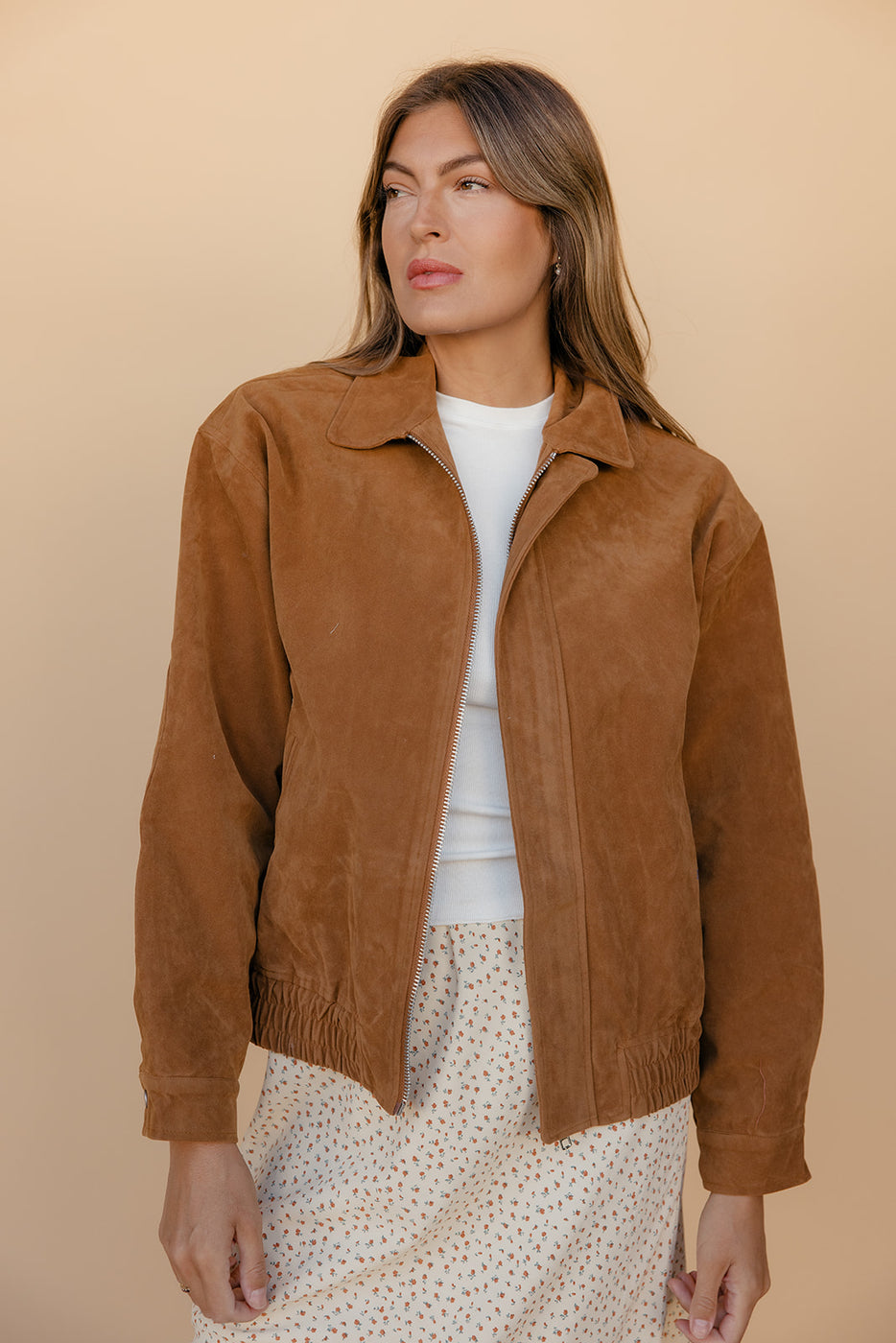Woman wearing a brown suede jacket against a beige background