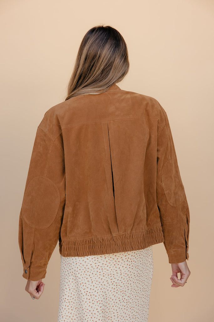 Person wearing a brown suede jacket on a beige background