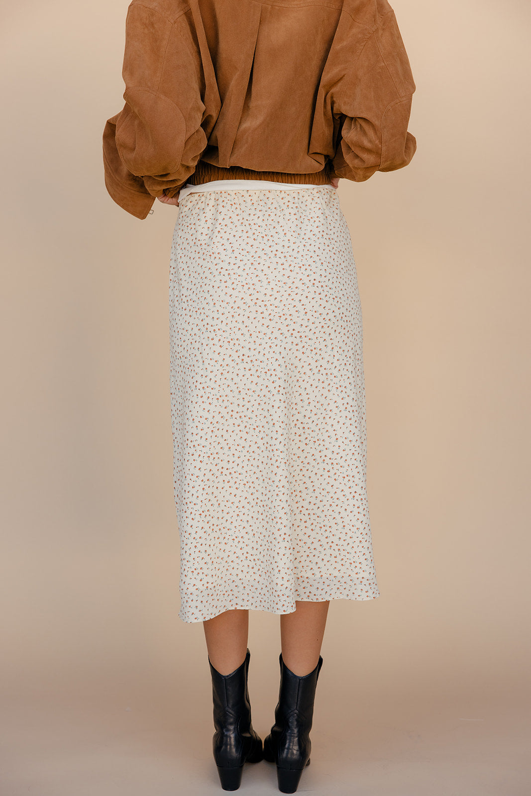 Person wearing a patterned skirt and brown top on a beige background
