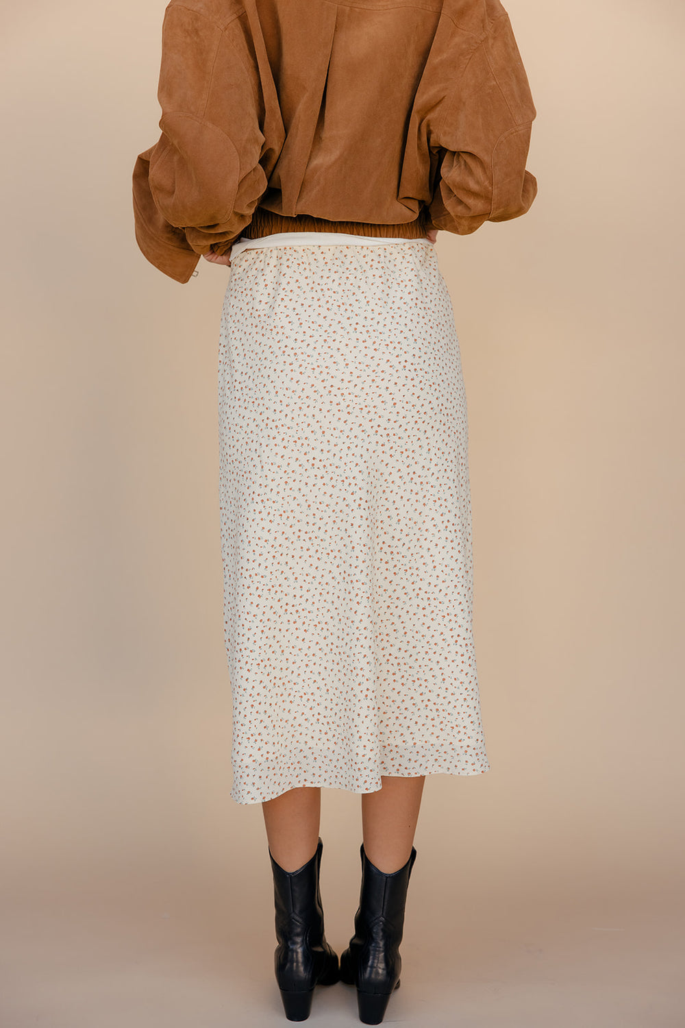 Person wearing a patterned skirt and brown top on a beige background