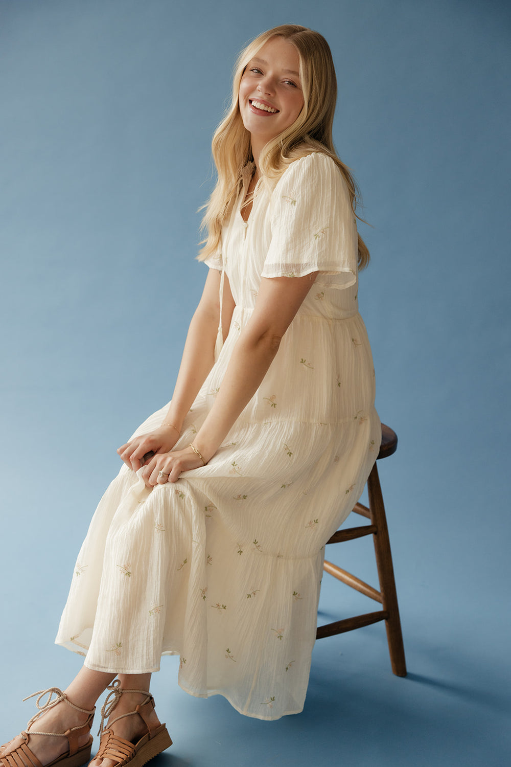 Woman in a white dress sitting on a wooden stool against a blue background