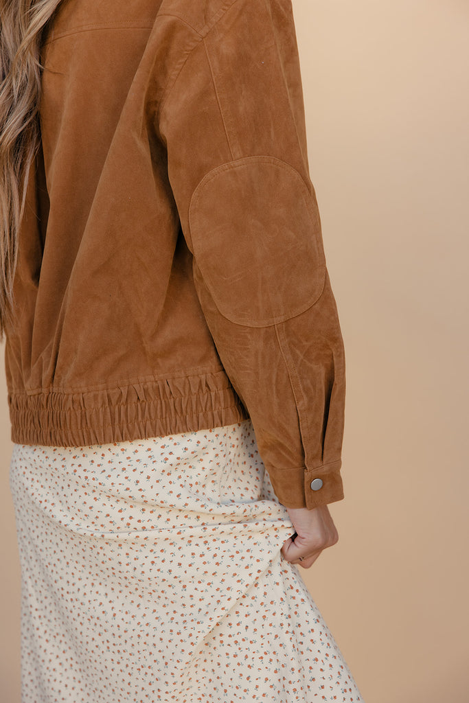 Brown suede jacket worn by a person on a beige background