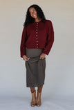 Woman wearing a burgundy sweater and plaid skirt against a plain background