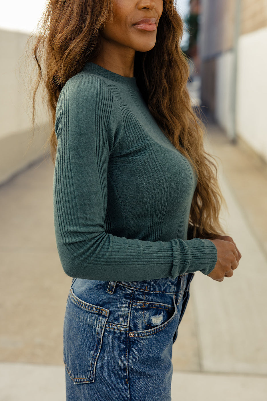 a woman with long hair wearing a green sweater and blue jeans