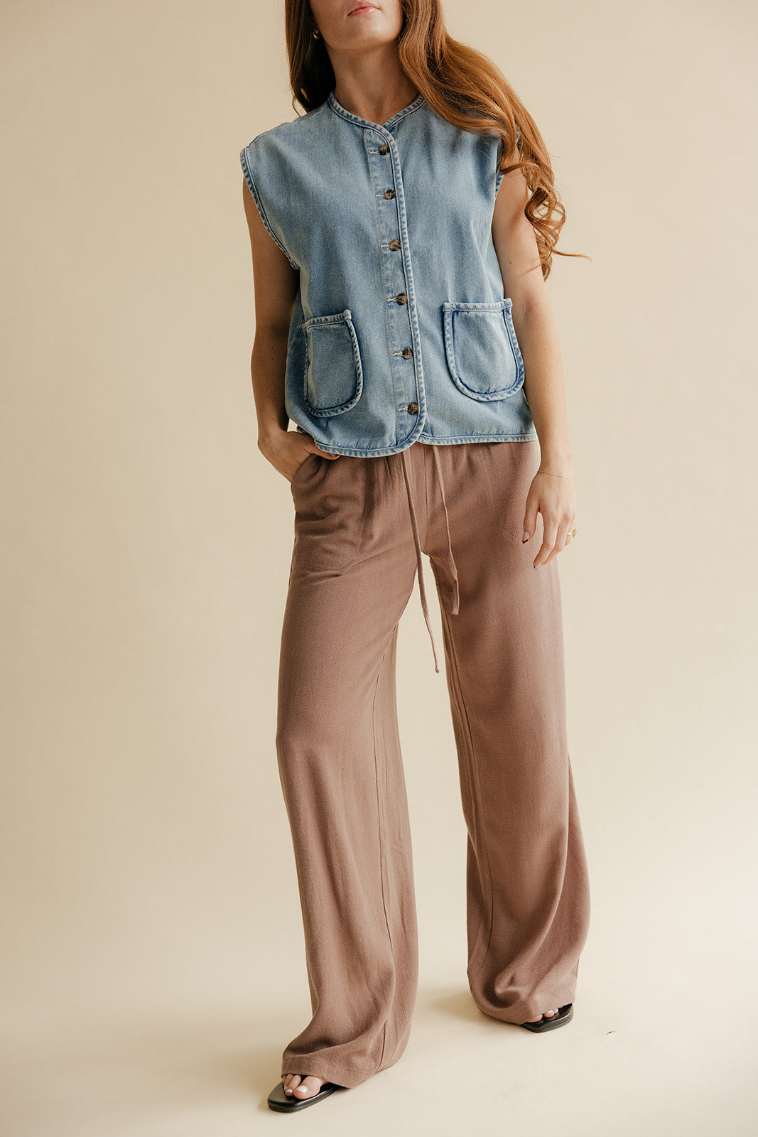Woman wearing a denim vest and brown pants on a beige background