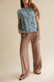 Woman wearing a denim vest and brown pants on a beige background