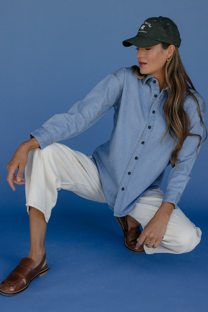 Woman in a blue shirt and white pants posing against a blue background