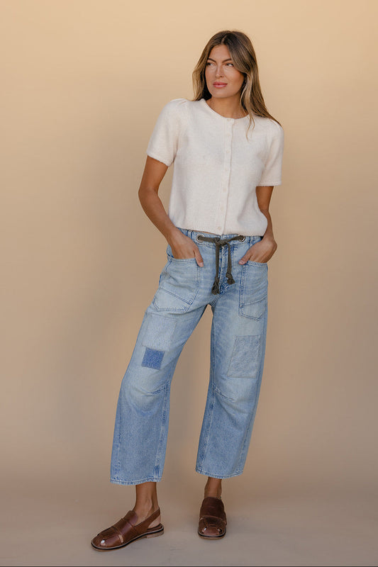Woman wearing a white blouse and blue jeans against a beige background