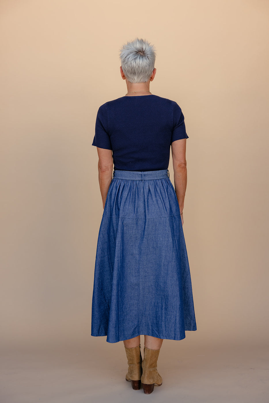Person wearing a navy top and blue skirt against a beige background
