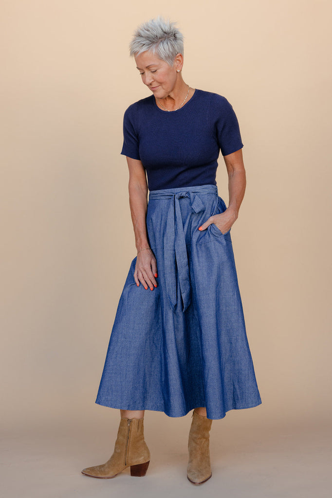 Woman wearing a blue top and denim skirt against a beige background