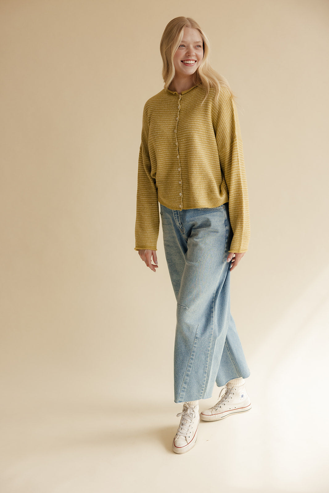 Woman wearing a mustard yellow shirt, light blue jeans, and white sneakers on a beige background