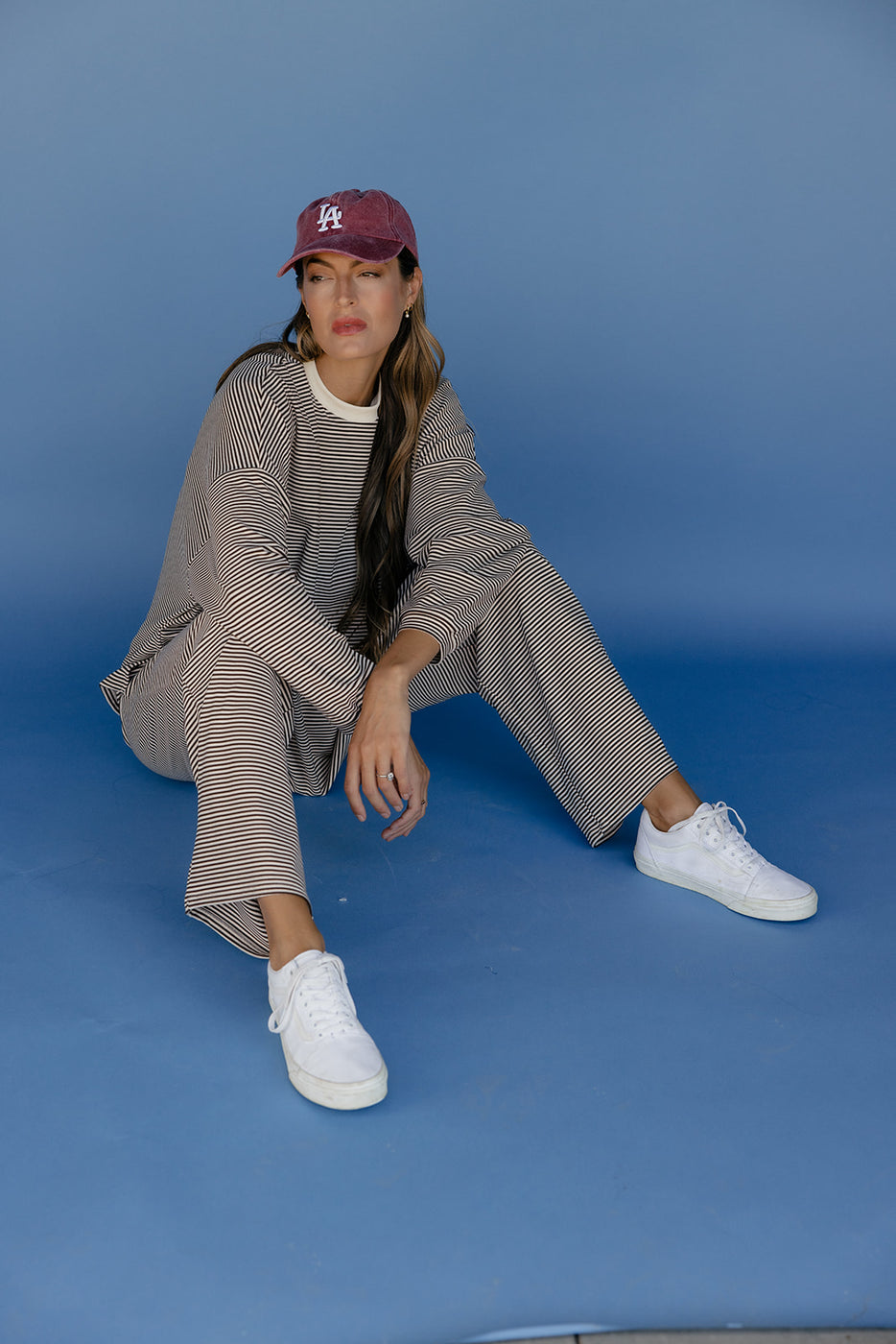 Woman wearing a gray outfit with white sneakers and a maroon cap against a blue background